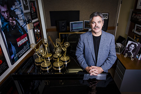 Award Winning Faculty' to 'A man in a light blue jacket with black shirt is posing with awards in a recording studio